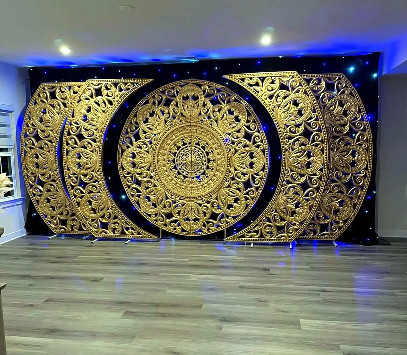 Ornate gold mandala backdrop panels on a black starlit drape with blue uplighting by Bsquare Events